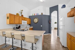 Eine Küche mit Holzschränken, einer weißen Mikrowelle, einem Spülbecken und einer Bar mit Hockern.