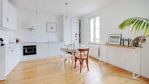 Een moderne keuken met witte kasten, een eettafel met stoelen en een groot raam dat voor natuurlijk licht zorgt.