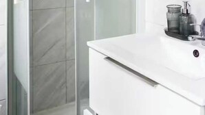 A modern bathroom with a glass shower enclosure, a white sink with a mirror above it, and a small cabinet below. - Cosy Studio - 2P- Clichy (Clichy)
