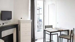 A modern room with a TV, a fireplace, a dining table with chairs, and a balcony with a view. - Cosy Studio - 2P- Clichy (Clichy)