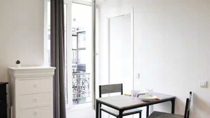 A small, bright room with a white dresser, a table with two chairs, and a door leading to a balcony. - Cosy Studio - 2P- Clichy (Clichy)