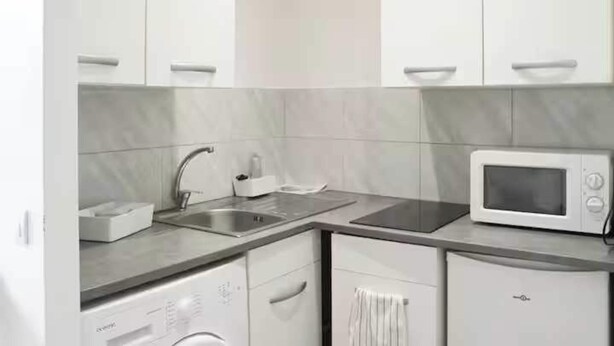 A modern kitchen with white cabinetry, a stainless steel sink, a microwave, and a dishwasher. - Cosy Studio - 2P- Clichy (Clichy)