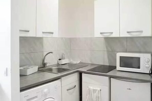 A modern kitchen with white cabinetry, a stainless steel sink, a microwave, and a dishwasher. - Cosy Studio - 2P- Clichy (Clichy)
