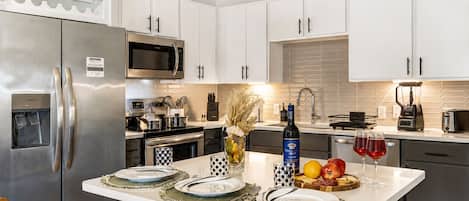 A modern kitchen with stainless steel appliances, white cabinetry, and a central island with a water dispenser and a bottle of wine.