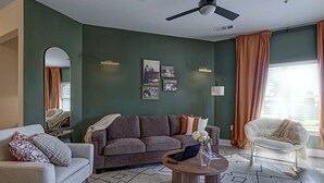 Una sala de estar con sofá, sillón, mesa de centro y una obra de arte en la pared.