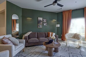 Una sala de estar con sofá, sillón, mesa de centro y una obra de arte en la pared.