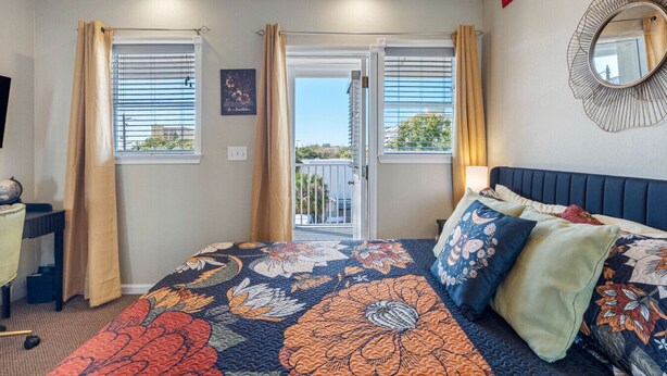 A bedroom with a large bed, two windows with curtains, a ceiling fan, and a view of the outside. - The Hive | Patio | Walk Downtown | Beach Gear (St. Petersburg)