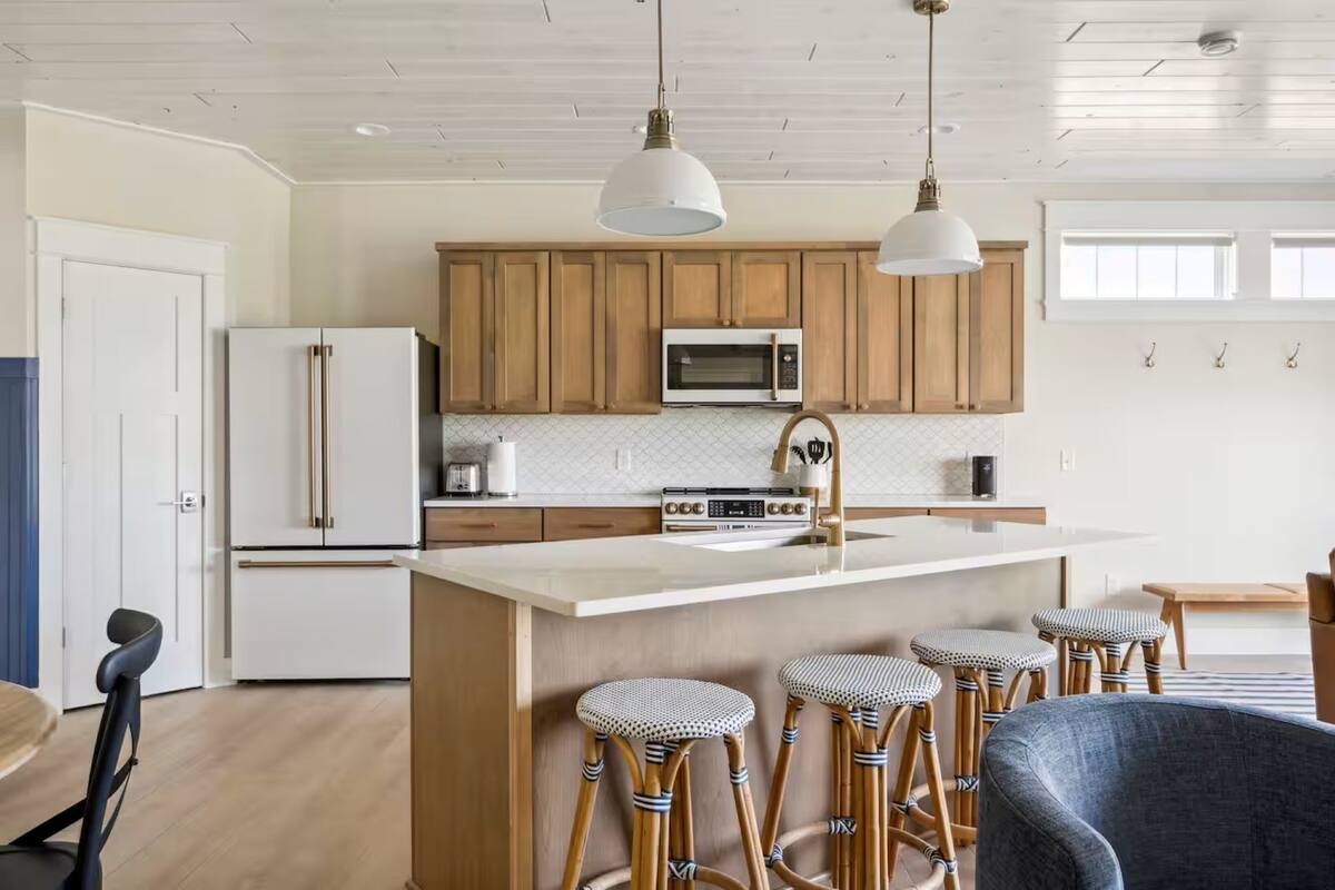 A modern kitchen with wooden cabinets, a white refrigerator, a microwave, and a large island with bar stools.