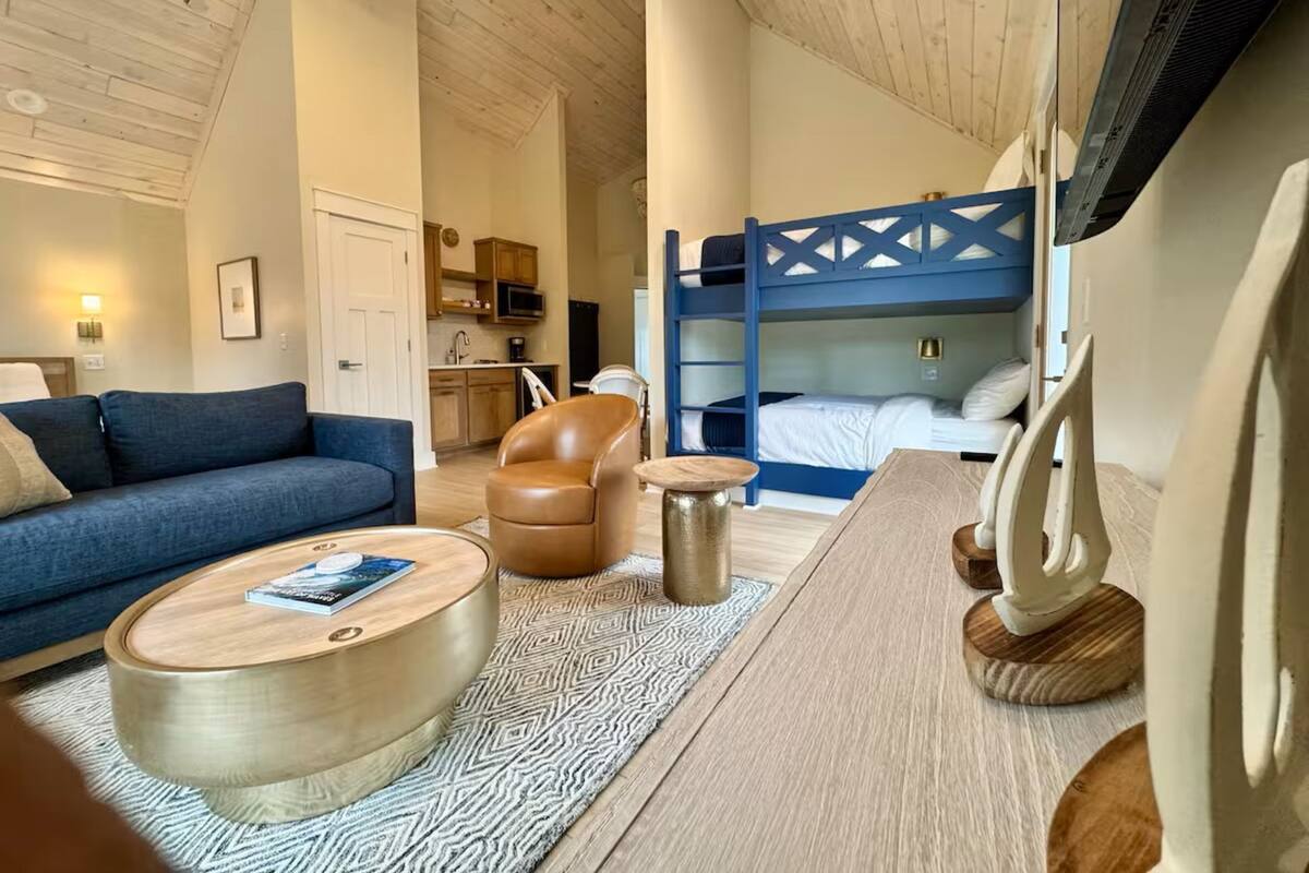 A modern interior with a sofa, a round coffee table, a leather armchair, a small side table, and a bunk bed with a blue headboard.