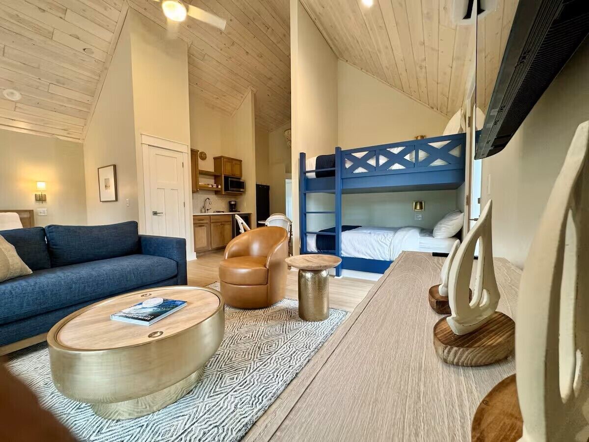 A cozy room with a blue sofa, a brown leather chair, a wooden coffee table, and a bunk bed with a blue headboard.