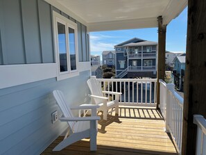 Eine Holzterrasse mit zwei weißen Adirondack-Stühlen, einem weißen Geländer und Blick auf benachbarte Häuser.