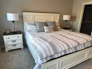 A bedroom with a bed, two bedside tables, a nightstand, a mirror, and a carpeted floor. - Harbor Splash | Steps to Indoor Pool (South Haven)