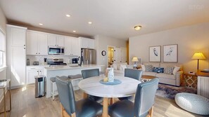 A modern kitchen with white cabinets, stainless steel appliances, and a dining area with a round table and chairs.