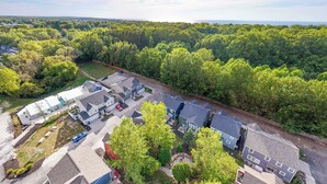 An aerial view of a residential area with houses, a parking lot, and a dense forest in the background. - Harbor Splash - Steps to Indoor Pool (South Haven)