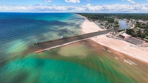 An aerial view of a coastal area with a long pier extending into the water, a sandy beach, and a town in the background. - Harbor Splash - Steps to Indoor Pool (South Haven)