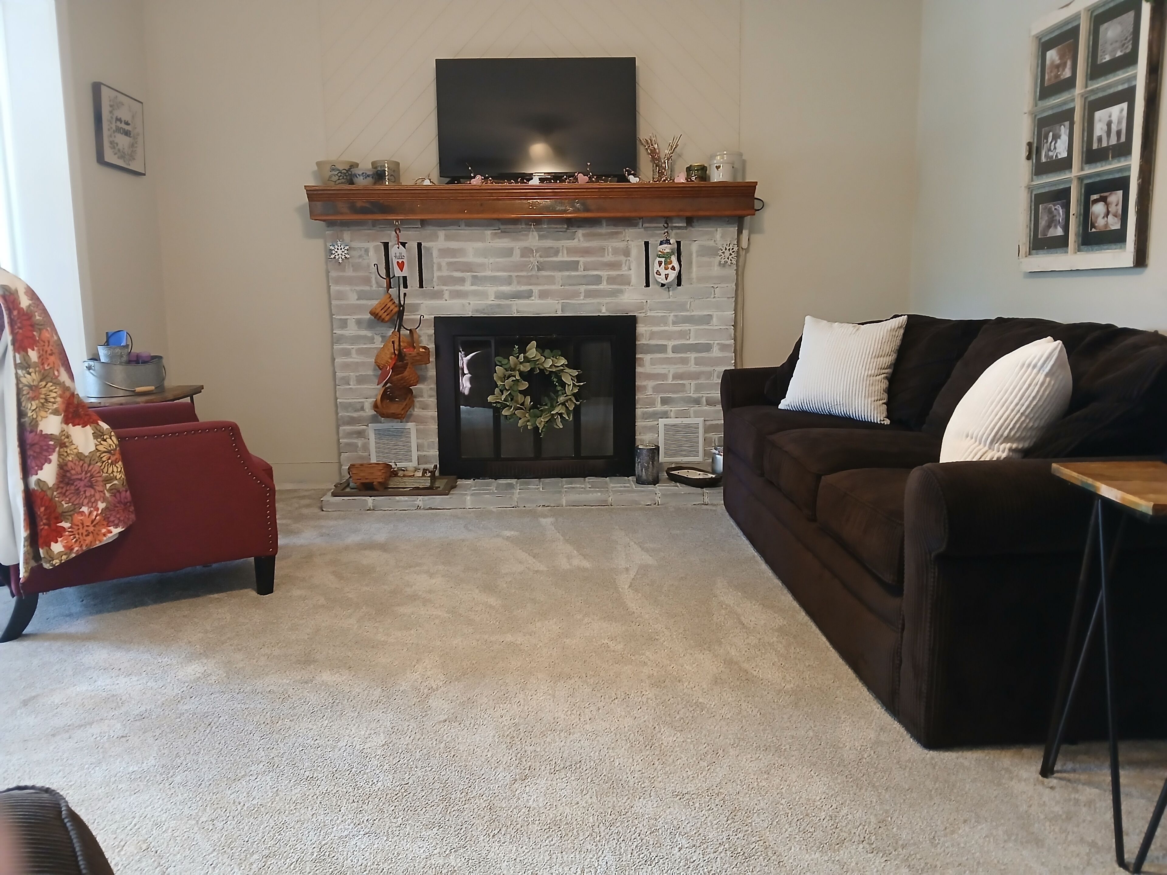 Una sala de estar con chimenea, un sof á, un sillón rojo y un televisor en la pared.