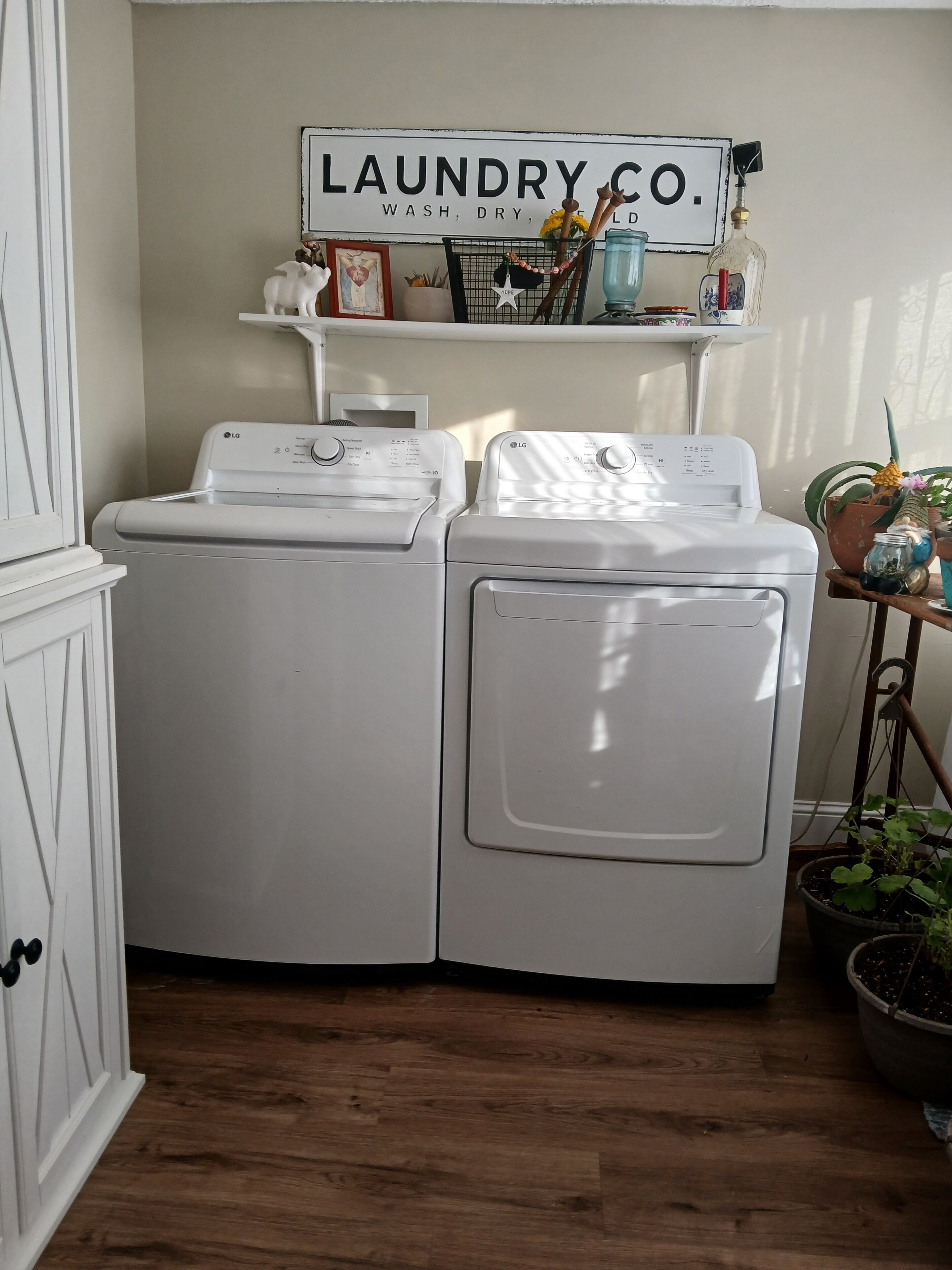 A laundry area with two white LG washing machines, a shelf with various items, and a sign that reads "LAUNDRY CO. WASH, DRY, FOLD".