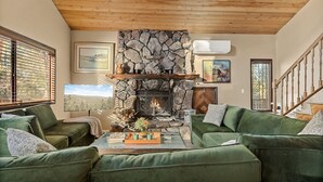 A cozy living room with a stone fireplace, green sofas, and a wooden ceiling. - Maple Lane w/ Hot Tub & EV charger, Pet Friendly (Big Bear)
