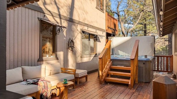 A cozy outdoor deck with a wooden staircase leading to a hot tub, a cushioned seating area, and a ship's wheel decoration. - Maple Lane w/ Hot Tub & EV charger, Pet Friendly (Big Bear)
