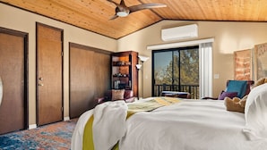 A bedroom with a large bed, a ceiling fan, a bookshelf, and a view of the outdoors through a window. - Maple Lane w/ Hot Tub & EV charger, Pet Friendly (Big Bear)