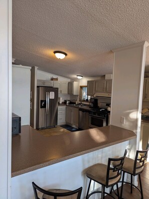 A kitchen with a central island, stainless steel appliances, and a bar seating area. - Cozy Lakehouse in Lawton (Lawton)