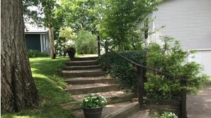 Una propiedad residencial con una escalera de piedra que conduce a una puerta principal, rodeada de abundante vegetación y plantas en macetas.
