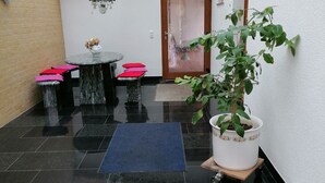 En pæn flisegulvsterrasse med træloft, et spisebord med lyserøde hynder og en potteplante.