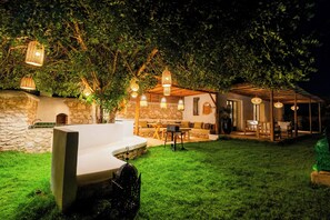 Ein gut beleuchteter Außenbereich mit Terrasse, einer Steinmauer, einer Holzpergola und hängenden Laternen.