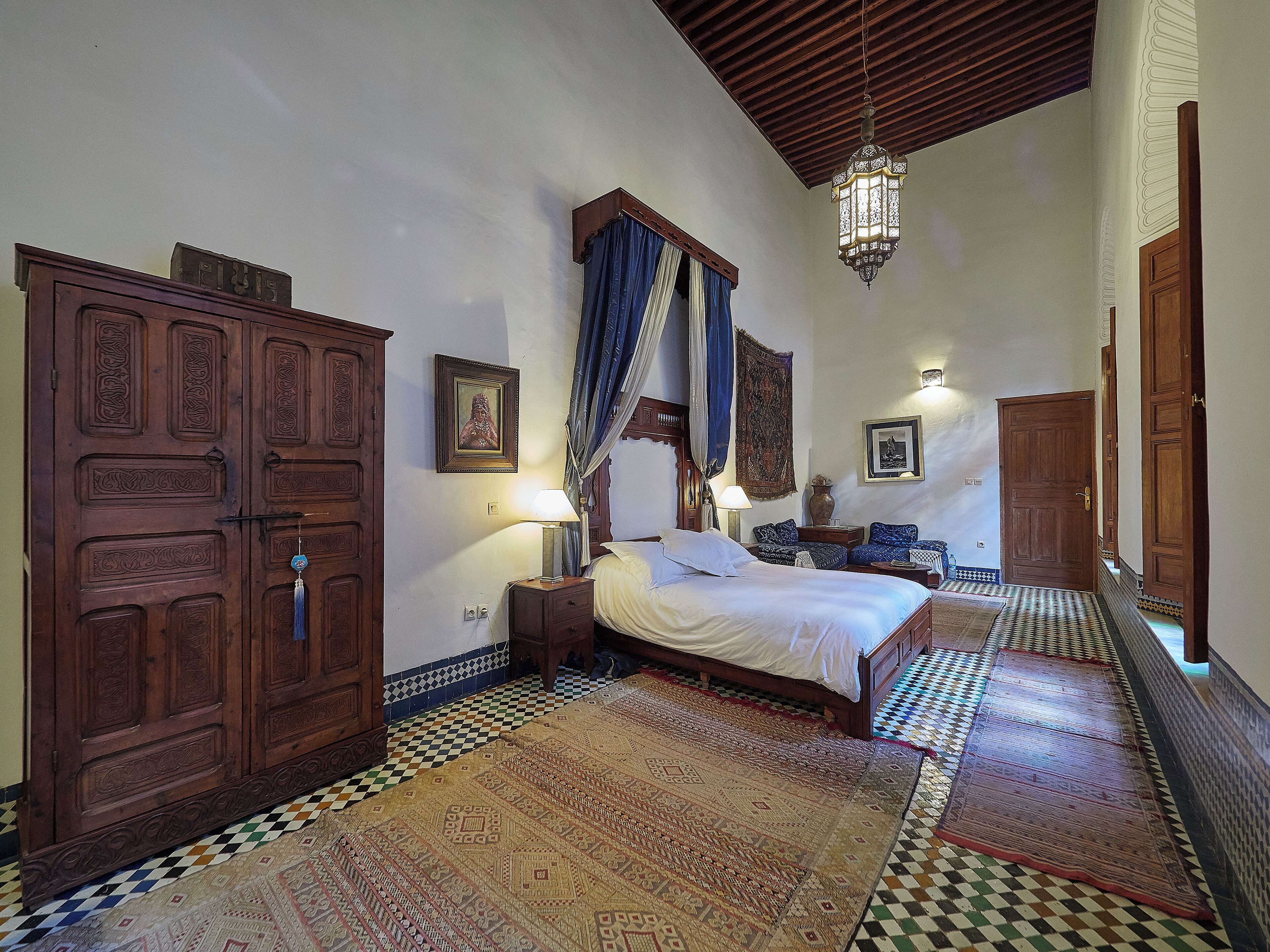 Une chambre de style traditionnel, dotée d’un grand lit, d’une armoire, d’une lanterne suspendue et de tapis à motifs.