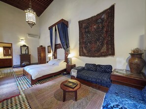 A traditional room with a bed, a sofa, a small table, and a large tapestry. - Dar Roumana (Fes)