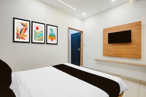 Ein Hotelzimmer mit einem Bett, einem an der Wand befestigten Fernseher und drei gerahmten Kunstwerken.