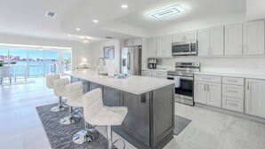 Una cocina moderna con armarios blancos, electrodomésticos de acero inoxidable y una isla central con taburetes de bar.