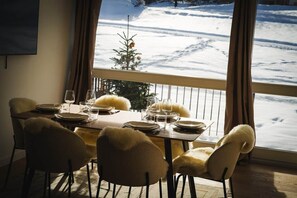 A dining table set for four with chairs, a view of a snowy landscape through a window, and a small Christmas tree. - The Courchevel Nests: APT 13, Le Praz (Courchevel)