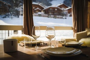 A dining table set with plates, glasses, and a mug, with a view of snow-covered buildings through a window. - The Courchevel Nests: APT 13, Le Praz (Courchevel)