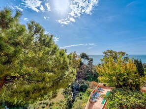 A coastal property with a pool and lounge chairs, surrounded by pine trees and other vegetation. - Apartment for 8, terrace, Wi-Fi, sea view (Roquebrune-Cap-Martin)