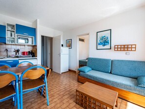 A compact living space with a kitchenette, a dining area with blue chairs, a sofa, and a coffee table. - Apartment for 8, terrace, Wi-Fi, sea view (Roquebrune-Cap-Martin)