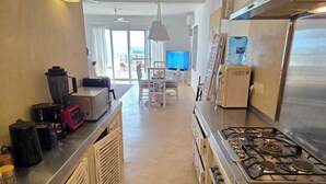 Une cuisine moderne équipée d’une cuisinière à gaz, d’un four à micro-ondes et d’un mixeur. On aperçoit un coin repas avec une table et des chaises au fond.