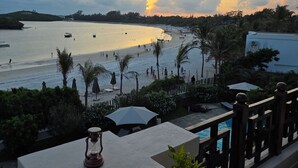 Une vue sur la mer avec une piscine, des palmiers et un coucher de soleil.