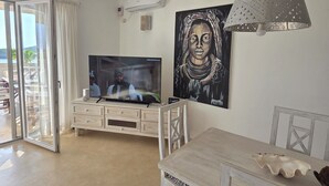 A modern living room with a flat-screen TV, a dining table with chairs, a pendant light, and a large framed artwork on the wall. - 200m² - Luxury Beachfront Apartment • Ocean View • 70m² Terrace • Watamu - Kenya (Watamu)