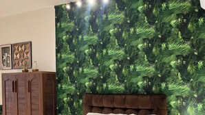 A bedroom with a bed, a wooden wardrobe, a nightstand, and a wall with a green leafy pattern. - Cozy 1BR with balcony and Nguyen Hue Walking Street view (Thành phố Hồ Chí Minh)