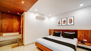 A modern bedroom with a wooden headboard, a large bed with black and white bedding, a nightstand, and a wall-mounted air conditioner.