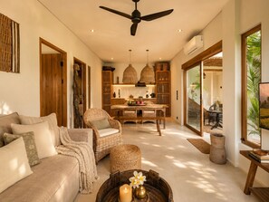 A spacious living area with a sofa, wicker furniture, a dining table with chairs, a ceiling fan, and a large window with a view of greenery. - Rice Field Villa with Rooftop Jacuzzi (Canggu)