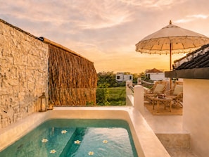 A rooftop pool with a stone wall, a hanging basket, and a lounge area with chairs and an umbrella. - Rice Field Villa with Rooftop Jacuzzi (Canggu)