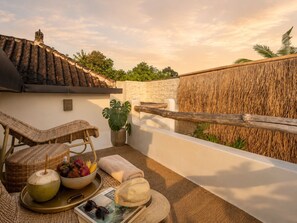 Ein Balkon mit Korbmöbeln, einem Topfpflanzen, einer Platte mit Früchten und einer Kokosnuss sowie einer Zeitschrift.