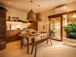 A modern kitchen with wooden cabinets, a dining table with wicker chairs, and a large window. - Rice Field Villa with Rooftop Jacuzzi (Canggu)