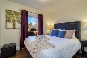 A bedroom with a large bed, a nightstand, a lamp, a window with curtains, and a wall decoration.