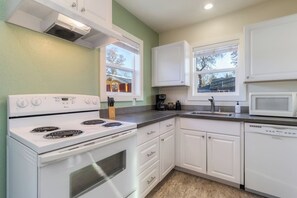 A kitchen with white cabinets, a stove, a microwave, and a sink.