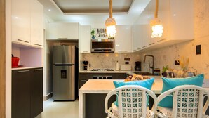 Una cocina moderna con muebles blancos, un refrigerador de acero inoxidable, horno empotrado y una lámpara colgante.