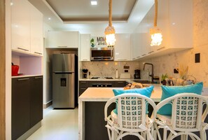 A modern kitchen with white cabinetry, a stainless steel refrigerator, a built-in oven, and a hanging light fixture. - Vista Cana | 3-Bedroom Villa with Private Pool (Bavaro)