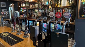 Un bar con varias griferías de cerveza, estantes llenos de botellas y una pizarra con la carta.